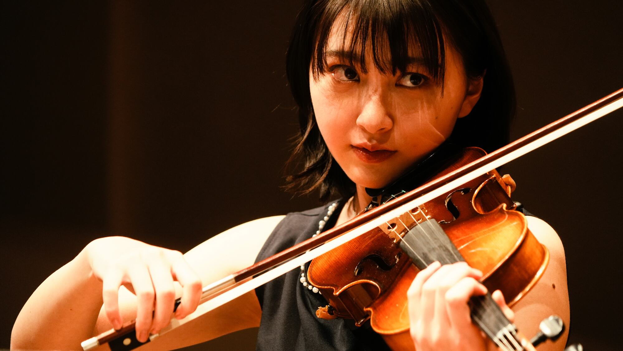 A young woman plays the violin in warm light