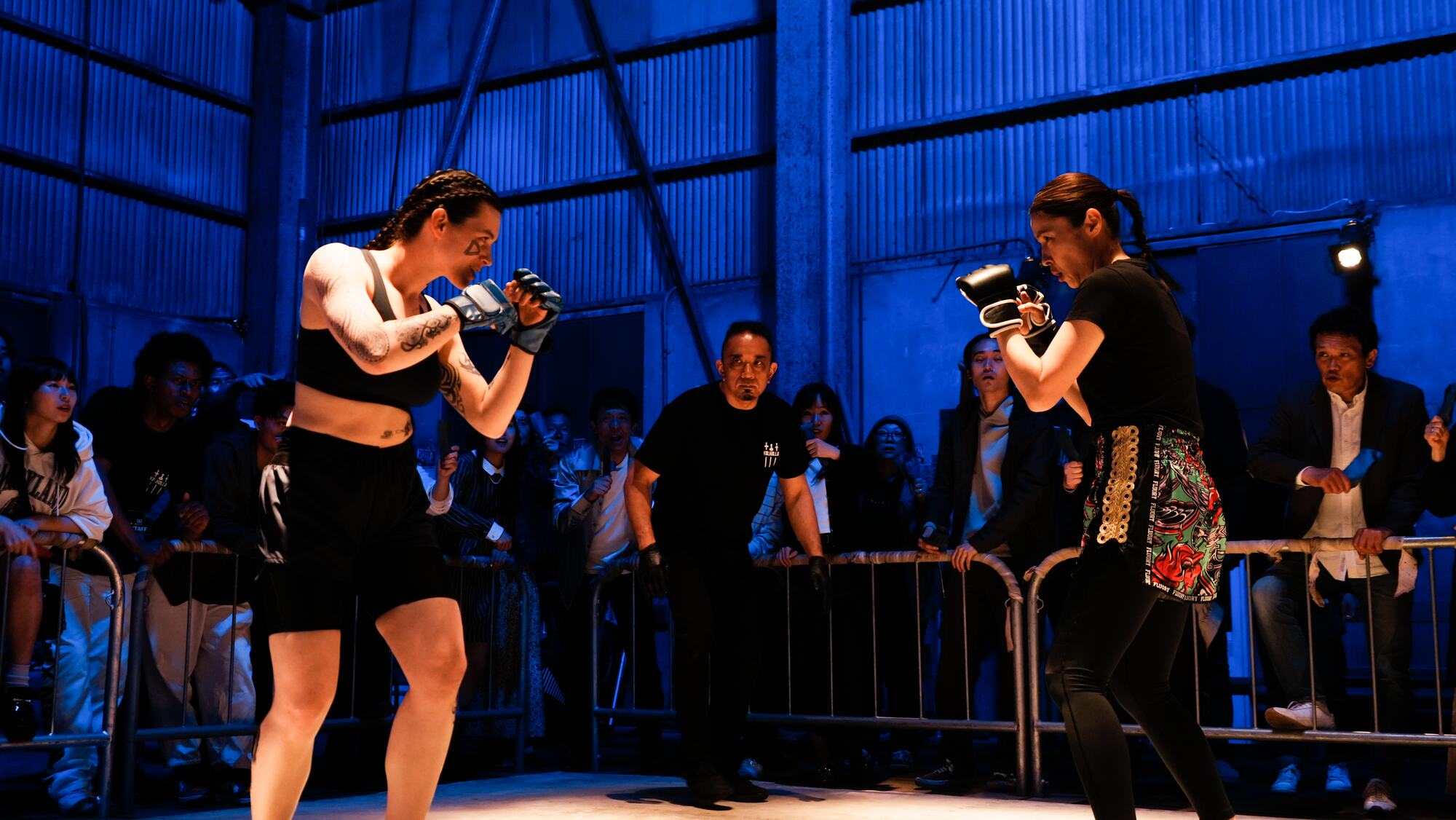 Two fighters square off under blue light as the crowd presses in