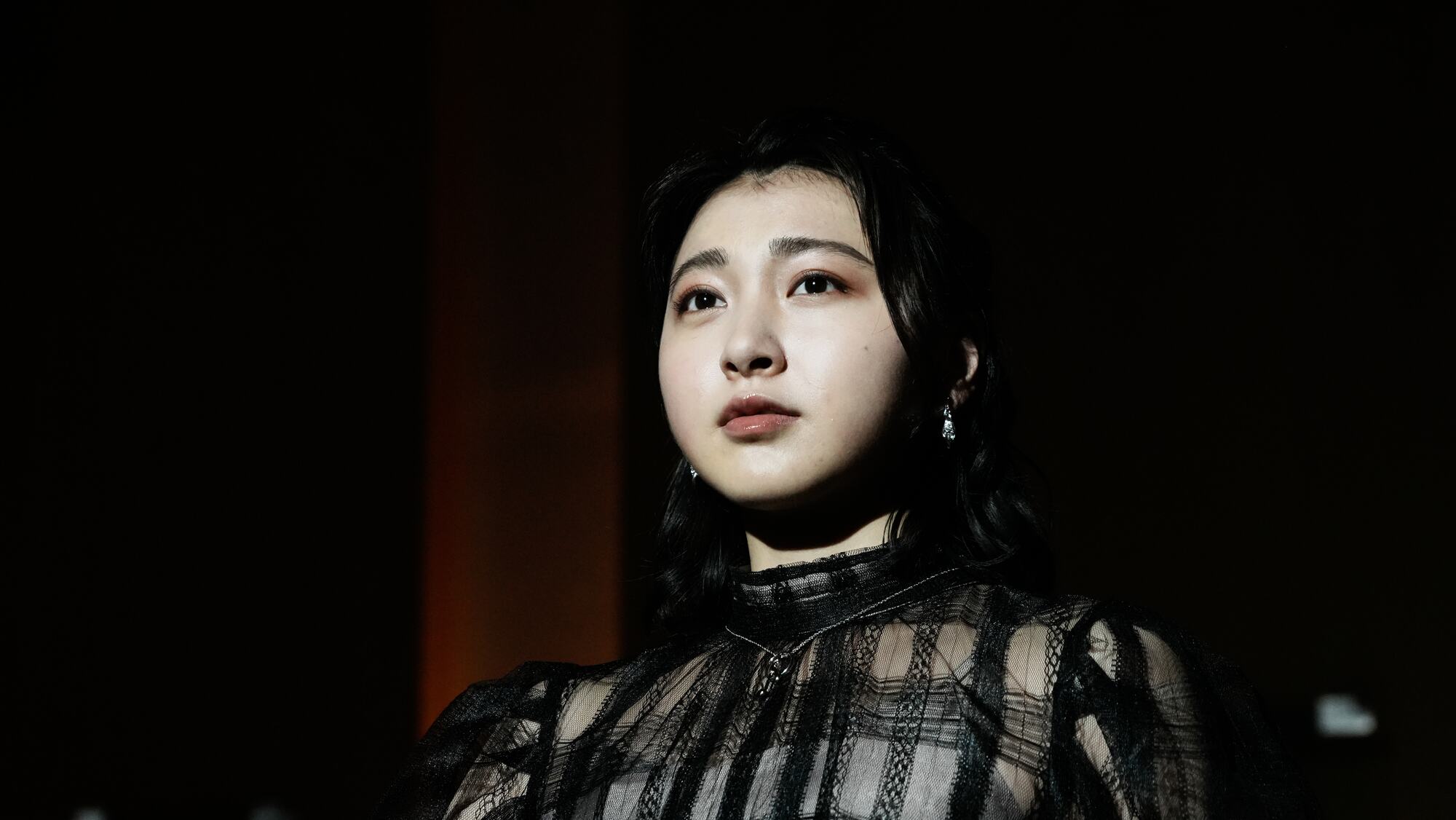 A young woman in black lace looks up into the light